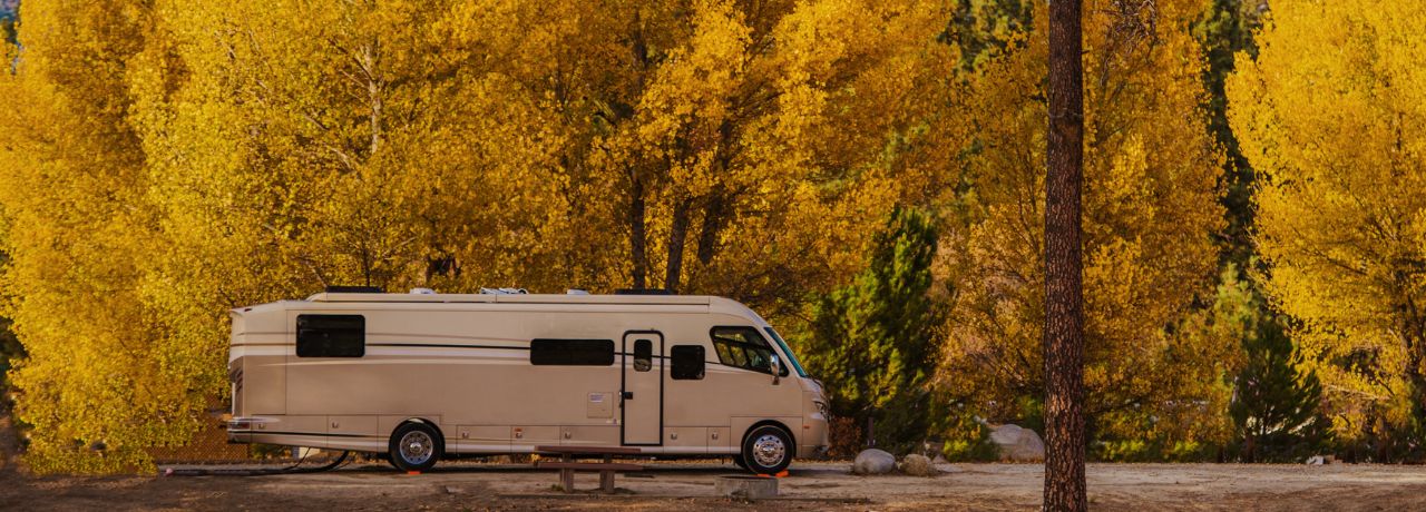 An RV parked in front of yellow fall foliage. Mountains can be seen in the distance.
